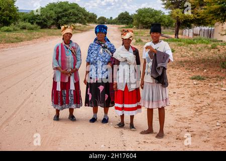 Gruppo di quattro donne boscimane di Kalahari centrale, villaggio New Xade in Botswana, a piedi su una strada sterrata Foto Stock