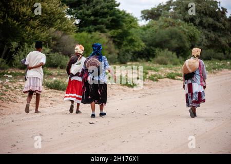 Gruppo di quattro donne boscimane di Kalahari centrale, villaggio New Xade in Botswana, a piedi su una strada sterrata Foto Stock