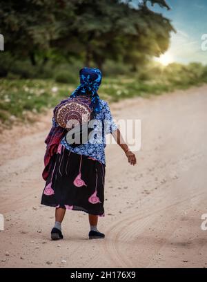 Vecchia donna bushman da Kalahari centrale, villaggio New Xade in Botswana, a piedi su una strada sterrata Foto Stock