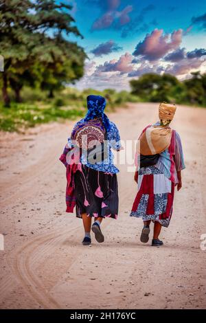 Due vecchie donne boscimane del Kalahari centrale, villaggio New Xade in Botswana, camminando su una strada sterrata Foto Stock