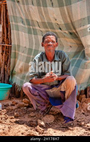Un vecchio boscimano di Kalahari centrale, villaggio New Xade in Botswana, di fronte al suo capanno Foto Stock