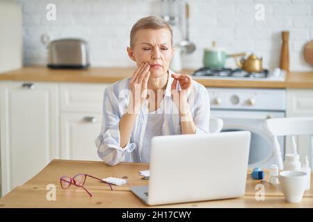 Donna matura frustrato che soffre di mal di denti mentre lavora in linea da casa Foto Stock