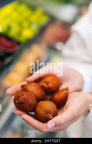 Primo piano verticale di una giovane donna adulta irriconoscibile che tiene in mano frutta fresca lychee. Foto Stock