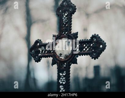 C'è una vecchia croce arrugginita nel cimitero, su cui appendono i rosari cattolici. Orrore alla caduta notturna. Segni religiosi. Foto Stock