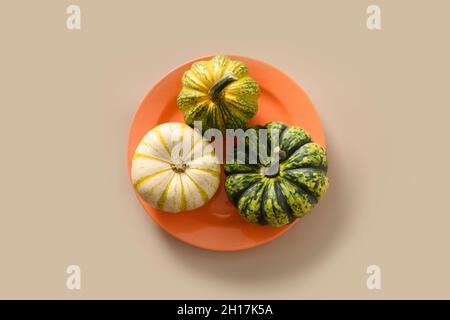 Concetto autunnale con tre zucche in piatti stagionali arancioni su sfondo beige. Vista dall'alto. Cena del giorno del Ringraziamento e tavolo. Foto Stock