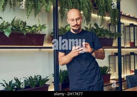 L'uomo d'affari concentrato utilizza lo smartphone con le cuffie mentre si trova in ufficio. Lavoro a distanza. Foto Stock