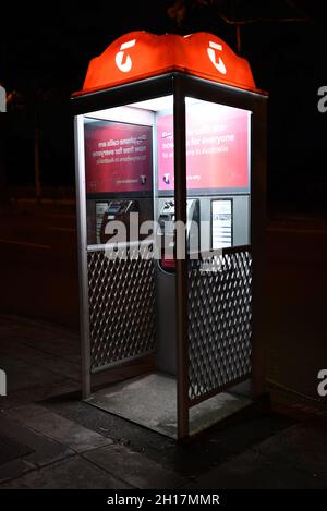 Un telefono a pagamento Telstra di notte, con la caratteristica illuminazione arancione sulla parte superiore dello stand Foto Stock