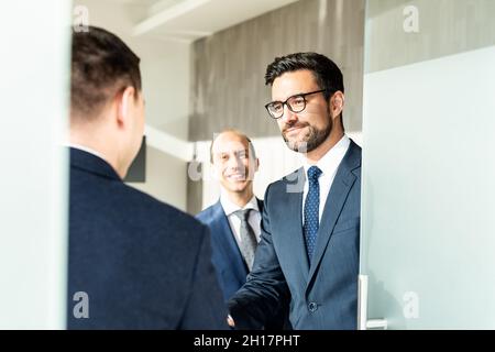 Gruppo di allegri uomini d'affari fiduciosi che salutano con una stretta di mano alla riunione d'affari in un ufficio moderno. Foto Stock
