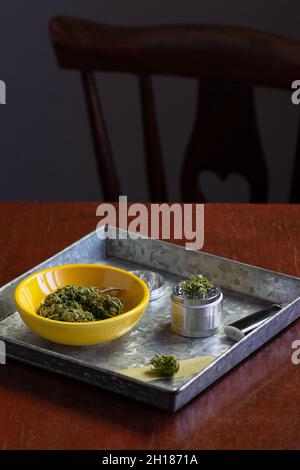 Germogli marijuana medici o fiori di canapa con macinacaffè di erbe e accessori di fumo in vassoio di metallo su tavola di legno Foto Stock