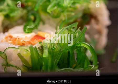 Delizioso sushi roll con formaggio Philadelphia, cetriolo, salmone e chuka in un vassoio di plastica su un tavolo di legno Foto Stock