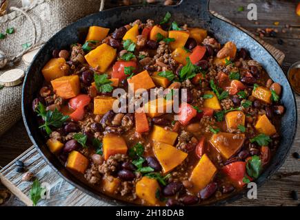 Stufato di manzo macinato con zucca di hokkaido e fagioli di rene in una deliziosa salsa di pomodoro e verdure. Servita in una padella rustica su sfondo di legno. Foto Stock