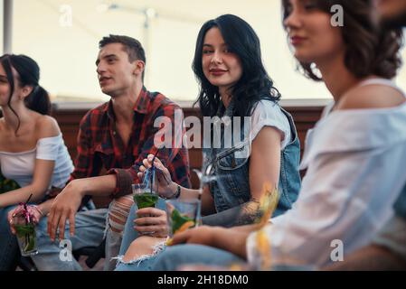 Una festa sul tetto. Giovani felici che bevono cocktail e chiacchierano seduti sul tetto Foto Stock