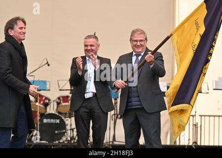 17 ottobre 2021, Baden-Wuerttemberg, Überlingen am Bodensee: Joachim Schuster (r), sindaco di Neuenburg am Rhein, detiene la bandiera dello spettacolo orticolo di Stato, che ha ricevuto da Manne Lucha (Bündnis90/Die Grünen, l), ministro dell'integrazione e degli Affari sociali a Baden-Württemberg, durante una cerimonia di fronte a centinaia di visitatori. L'anno prossimo, nel 2022, Neuenburg am Rhein ospiterà lo state Garden Show. In tale contesto è Gerhard Hugenschmidt (centro), presidente dell'assemblea degli azionisti della Förderungsgesellschaft für die Baden-Württembergischen Landesgartenschauen mbH. Foto: Feli Foto Stock