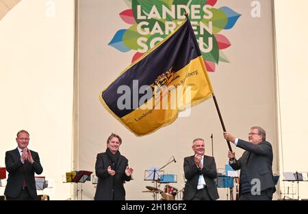 17 ottobre 2021, Baden-Wuerttemberg, Überlingen am Bodensee: Joachim Schuster (r), sindaco di Neuenburg am Rhein, detiene la bandiera dello spettacolo orticolo di Stato, che ha ricevuto da Manne Lucha (Bündnis90/Die Grünen, 2° da sinistra), Ministro dell'integrazione e degli Affari sociali a Baden-Württemberg, durante una cerimonia di fronte a centinaia di visitatori. L'anno prossimo, nel 2022, Neuenburg am Rhein ospiterà lo state Garden Show. Sullo sfondo è Gerhard Hugenschmidt (3° da sinistra), presidente dell'assemblea dei soci del Förderungsgesellschaft für die Baden-Württembergischen Landesgartenschau Foto Stock