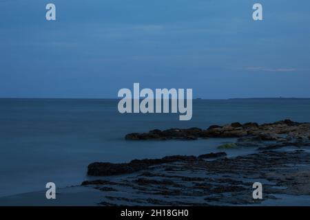 LUNGA ESPOSIZIONE NOTTURNA, IMMAGINE DEL CIELO DRAMTIC E ONDA DI MARE CON ROCCIA IN SFONDO SCENARIO. Foto Stock