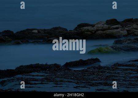 LUNGA ESPOSIZIONE NOTTURNA, IMMAGINE DEL CIELO DRAMTIC E ONDA DI MARE CON ROCCIA IN SFONDO SCENARIO. Foto Stock