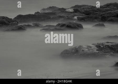 LUNGA ESPOSIZIONE NOTTURNA, IMMAGINE DEL CIELO DRAMTIC E ONDA DI MARE CON ROCCIA IN SFONDO SCENARIO. Foto Stock