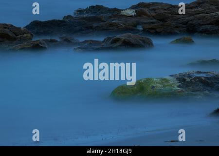 LUNGA ESPOSIZIONE NOTTURNA, IMMAGINE DEL CIELO DRAMTIC E ONDA DI MARE CON ROCCIA IN SFONDO SCENARIO. Foto Stock