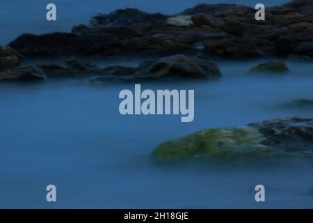 LUNGA ESPOSIZIONE NOTTURNA, IMMAGINE DEL CIELO DRAMTIC E ONDA DI MARE CON ROCCIA IN SFONDO SCENARIO. Foto Stock