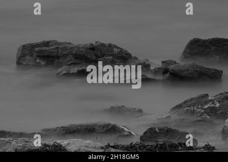 LUNGA ESPOSIZIONE NOTTURNA, IMMAGINE DEL CIELO DRAMTIC E ONDA DI MARE CON ROCCIA IN SFONDO SCENARIO. Foto Stock