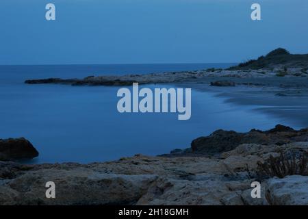 LUNGA ESPOSIZIONE NOTTURNA, IMMAGINE DEL CIELO DRAMTIC E ONDA DI MARE CON ROCCIA IN SFONDO SCENARIO. Foto Stock