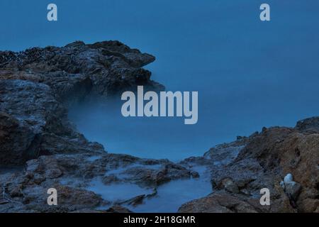 LUNGA ESPOSIZIONE NOTTURNA, IMMAGINE DEL CIELO DRAMTIC E ONDA DI MARE CON ROCCIA IN SFONDO SCENARIO. Foto Stock