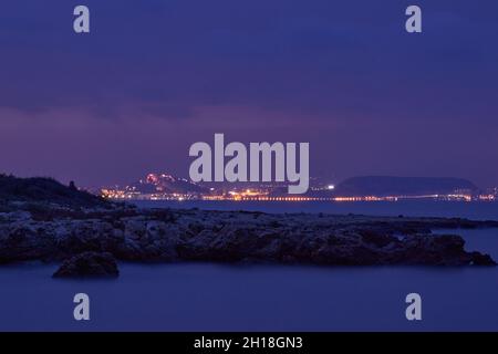 LUNGA ESPOSIZIONE NOTTURNA, IMMAGINE DEL CIELO DRAMTIC E ONDA DI MARE CON ROCCIA IN SFONDO SCENARIO. Foto Stock