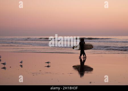 I surfisti gettano un'ombra sulla sabbia bagnata mentre camminano su Huntington Beach al tramonto. Huntington Beach, California, Stati Uniti. Foto Stock