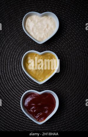 Ciotole a forma di cuore con ketchup, maionese e salsa di senape, colpo verticale. Foto Stock