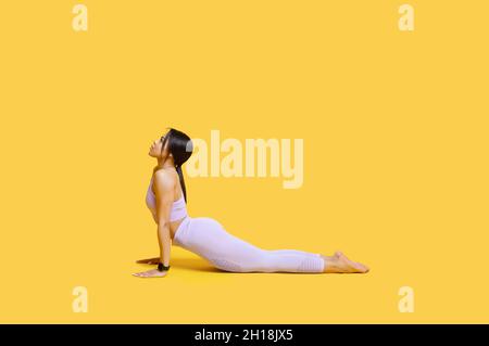 Allenarsi. Giovane donna nera che pratica yoga, facendo esercizio Cobra, rimanendo in posa Bhujangasana, sfondo giallo Foto Stock