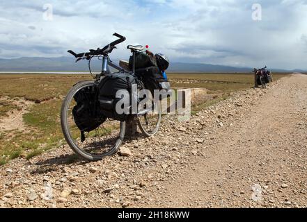 Strada sterrata e due biciclette vicino al lago Son-Kul e alle montagne del Kirghizistan Foto Stock