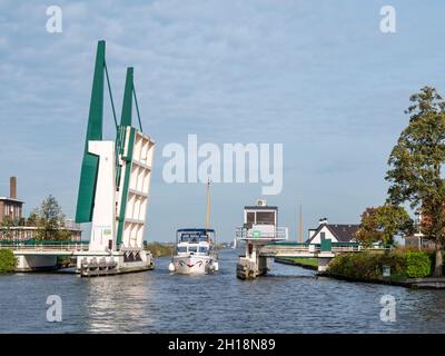 Yacht a motore che passa il ponte levatoio Osingahuizen sopra l'ampio canale di Wimerts in Friesland, Olanda Foto Stock