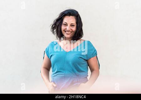 Donna di mezza età sicura, bruna in piedi e sorridente Foto Stock