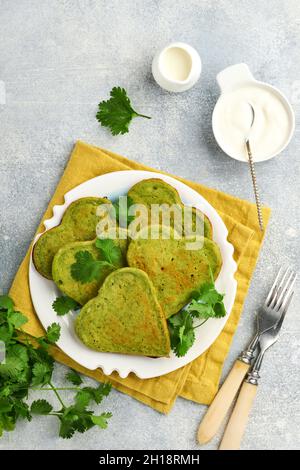 Frittelle all'avocado di spinaci a forma di cuore con salsa allo yogurt greco e pomodori ciliegini su piatto bianco su sfondo grigio chiaro. Cibo per la colazione Foto Stock