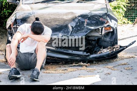 Disperato uomo che piange sulla sua vecchia auto danneggiata dopo un incidente Foto Stock