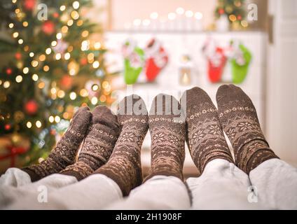 Tre paia di diverse età delle gambe in calze di lana. A Natale, di fronte ad un albero di Natale decorato e calze regalo appesi su un comò. Foto Stock