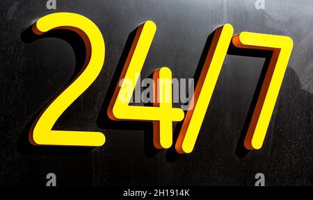 24 ore giallo segno aperto o di lavoro intorno all'orologio appeso su parete scura. Apri cartello. Lavoro diurno e notturno. 24 ore concetto Foto Stock