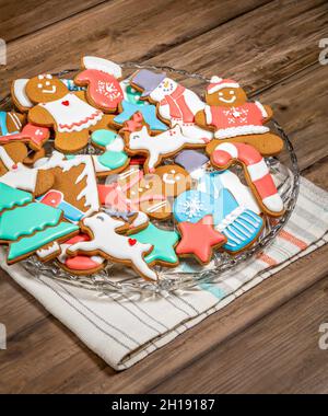 Biscotti di Natale di Gingerbread decorati in modo luminoso e colorato su un piatto con sfondo in legno. Foto Stock