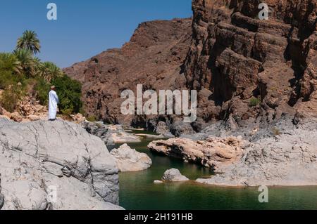 Un uomo che guarda fuori su una piscina naturale in Wadi al Arbeieen. Wadi al Arbeieen, Oman. Foto Stock