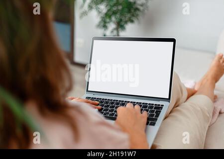 Woman looking at mockup white laptop computer screen on online e learning app web site or moovie at home. Over shoulder close up female hands on Foto Stock