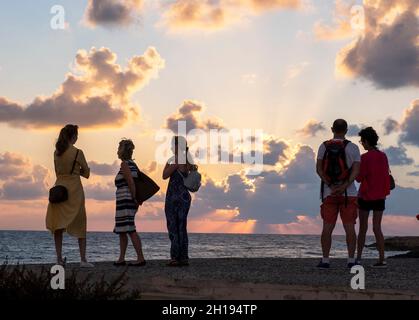I turisti guardare il sole che tramonta al porto di Paphos, Cipro. Foto Stock