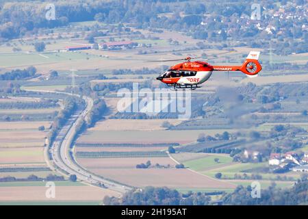 Waldkirch, Germania. 15 ottobre 2021. Un elicottero di soccorso della DRF Luftrettung vola in aria mentre un'autostrada federale a più corsie può essere vista sullo sfondo. Durante l'addestramento del verricello, l'equipaggio della stazione di Friburgo della DRF Luftrettung (cartello di chiamata Christoph 54) pratica le operazioni con il verricello sotto un elicottero insieme al Black Forest Mountain Rescue Service. Questo verricello può essere utilizzato per salvare i pazienti da terreni impraticabili, nonché per trasportare medici e paramedici in regioni difficili da raggiungere. Credit: Rin/dpa/Alamy Live News Foto Stock