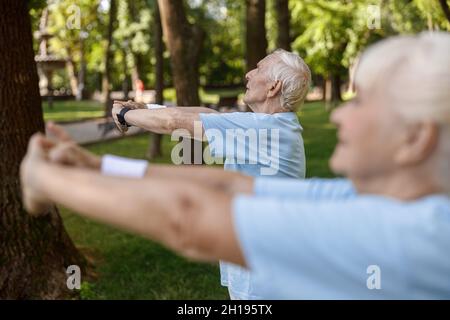 Uomo maturo grigio con capelli si allena con donna sul prato nel parco cittadino Foto Stock