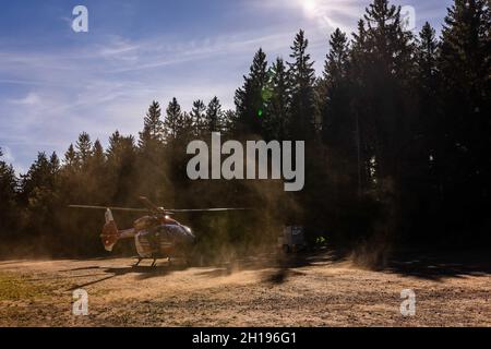 Waldkirch, Germania. 15 ottobre 2021. Un elicottero di soccorso della DRF Luftrettung soffia la polvere con i suoi rotori su un parcheggio per escursionisti. Durante l'addestramento del verricello, l'equipaggio della stazione di Friburgo della DRF Luftrettung (cartello di chiamata Christoph 54) pratica le operazioni con il verricello sotto un elicottero insieme al Black Forest Mountain Rescue Service. Questo verricello può essere utilizzato per salvare i pazienti da terreni impraticabili, nonché per trasportare medici e paramedici in regioni difficili da raggiungere. Credit: Rin/dpa/Alamy Live News Foto Stock