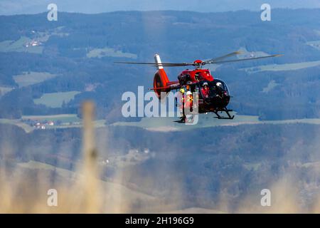 15 ottobre 2021, Baden-Wuerttemberg, Waldkirch: Un membro ciascuno del Bergwacht e del DRF Luftrettung si trova sulle piste di un elicottero di salvataggio, mentre la Foresta Nera può essere visto in background. Durante l'addestramento del verricello, l'equipaggio della stazione di Friburgo della DRF Luftrettung (cartello di chiamata Christoph 54) pratica le operazioni con il verricello sotto un elicottero insieme al Black Forest Mountain Rescue Service. Questo verricello può essere utilizzato per salvare i pazienti da terreni impraticabili, nonché per trasportare medici e paramedici in regioni difficili da raggiungere. Foto: Philipp von Ditfurth/dpa Foto Stock