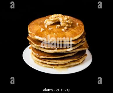 Una pila di pancake con miele e noci su sfondo nero. Foto Stock