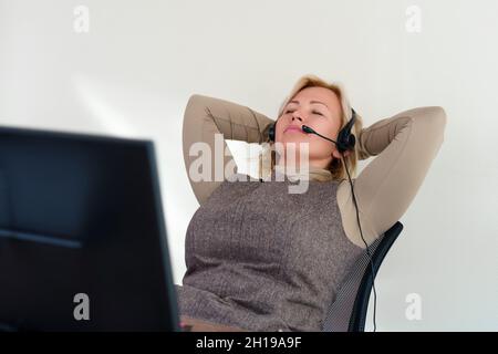 Donna d'affari che si rilassa con le mani dietro la testa e seduta su una sedia da ufficio di fronte al computer. Foto Stock
