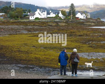 Il paesaggio autunnale della Scozia: Una coppia anziana cammina il loro cane sulla costa di Loch Carron nel pittoresco villaggio scozzese di Plockton. Foto Stock