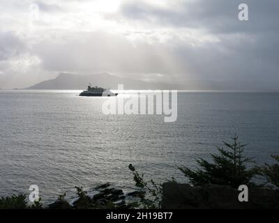 Scena suggestiva dall'isola di Skye guardando indietro verso la terraferma scozzese con una nave da crociera ormeggiata al mare e la luce del sole che si infrangono attraverso la nuvola. Foto Stock