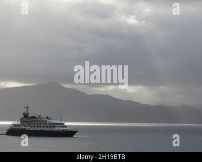 Atmosfera della Scozia: Nave da crociera MS Island Sky al largo dell'isola di Skye con luce solare applesa sull'acqua e toni di grigio sulle colline e nel cielo. Foto Stock